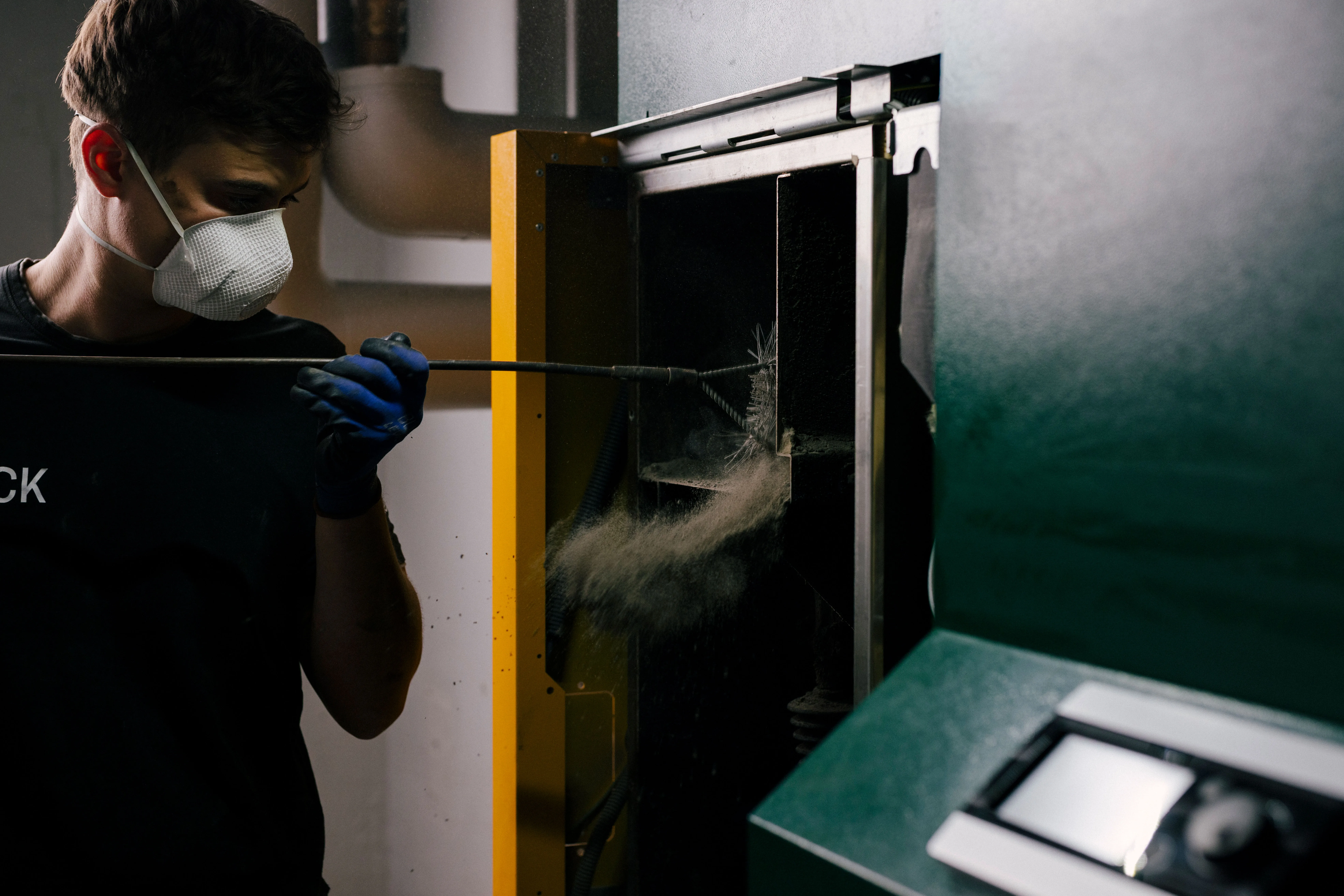 Ein Kundendienst-Techniker reinigt eine Pelletheizung im Technikraum während einer professionellen Heizungswartung.