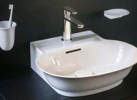 Ein weißes, modern geformtes Waschbecken der Marke "Laufen" ist mit einem verchromten Wasserhahn ausgestattet. 