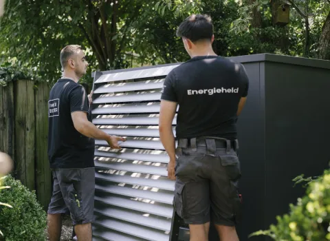 Zwei Anlagenmechaniker der Firma Frick stehen im Garten vor einer großen Waermepumpe.