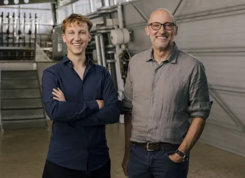 Die beiden Geschäftsführer der Firma Frick stehen in der Werkstatt und lächeln in die Kamera.