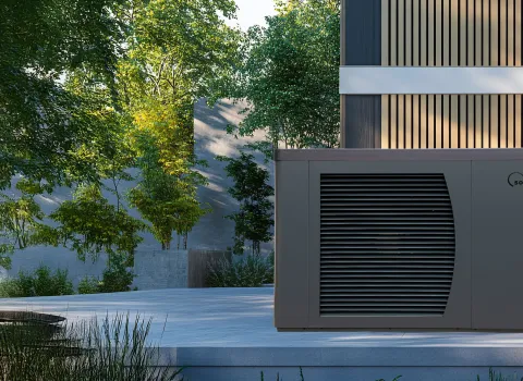 Eine Solvis-Wärmepumpe mit Lamellenfront steht auf einer Terrasse neben einem modernen Holzfassadenhaus, umgeben von Bäumen und Natur.