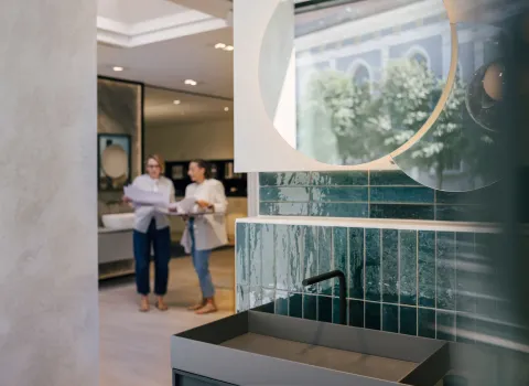 Moderne Waschtischanlage in einer Badausstellung, im Hintergrund beraten zwei Fachberaterinnen Kunden zur Badplanung.