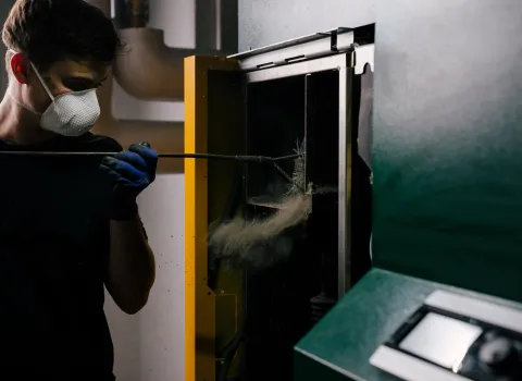 Ein Kundendienst-Techniker reinigt eine Pelletheizung im Technikraum während einer professionellen Heizungswartung.