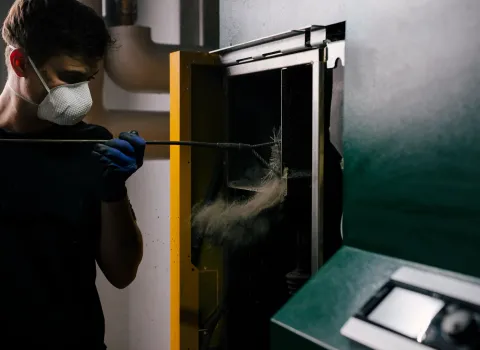 Ein Kundendienst-Techniker reinigt eine Pelletheizung im Technikraum während einer professionellen Heizungswartung.